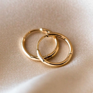 Detaillierte Makroansicht polierter goldener Creolen auf elegantem Seidenhintergrund