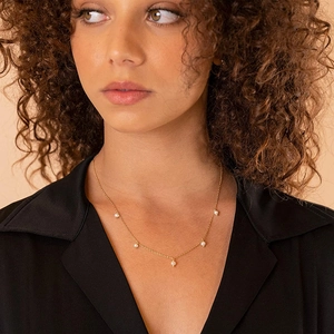 Close-up of minimalist gold chain necklace with five elegant white pearls on a model