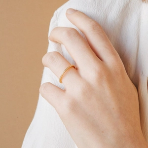 Elegant gold eternity ring with micro-pave diamonds on model finger against warm background