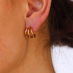 Close-up of triple-layered golden C-shaped hoop earrings worn on a female ear