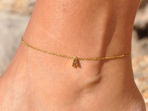 Close-up of a delicate gold anklet with a 3D letter A pendant on a woman's ankle