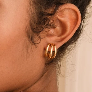 Close-up of triple-layered golden C-shaped hoop earrings worn on a model's ear