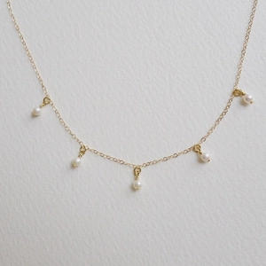 Detail view of thin gold-plated chain necklace featuring five evenly spaced white pearls