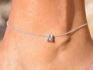 Detail shot of a silver stainless steel anklet with a minimalist letter M pendant