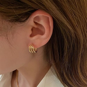 Close-up of golden triple-layered C-shaped hoop earrings worn by a model in warm light