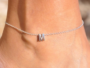 Macro shot of silver stainless steel ankle chain featuring a polished letter M pendant