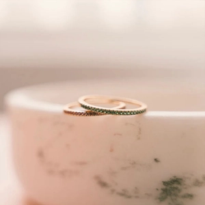 Detail view of two rose gold eternity rings with emerald green and deep red stones