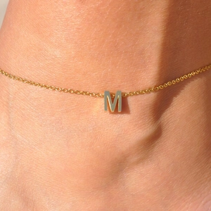 Detailed close-up of a gold M letter pendant worn on an elegant thin cable chain
