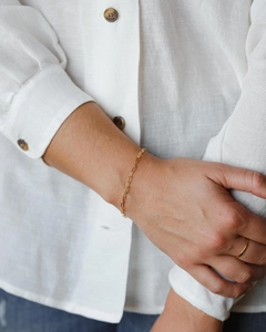 Detail eines minimalistischen vergoldeten Kettengliedarmbands an einem Leinenärmel