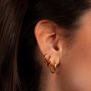Detailed view of three high-polished gold hoop earrings on model to show sizing