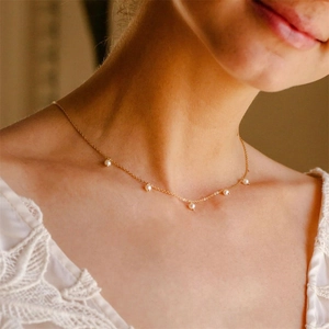 Close-up of a gold necklace with five white pearls on a model neck with lace dress