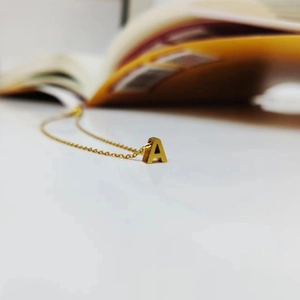 Macro shot of minimalist gold initial A pendant on a fine curb chain against white backdrop
