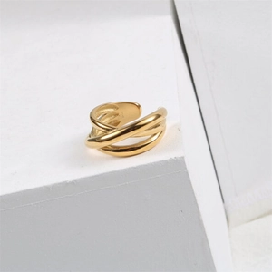 Détail d'une bague multicouche dorée croisée sur un support géométrique blanc épuré