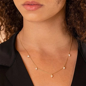 Close-up of a gold link necklace with five white pearls worn by a model in a black blazer