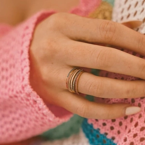 Macro shot of five stacked gold rings with colorful pavé gemstones on model hand