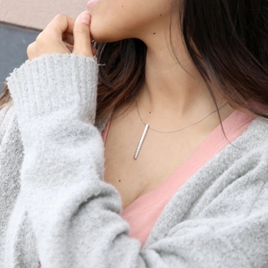 Close-up of minimalist silver rectangular bar pendant with Roman numeral engraving