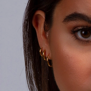 Set of three polished gold plated stainless steel hoop earrings worn on a model's ear