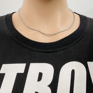Collier chaîne en corde argentée porté sur un haut noir pour un style minimaliste