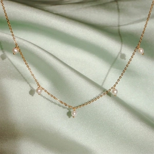 Detail view of a gold pearl necklace with five pearls on a green silk background