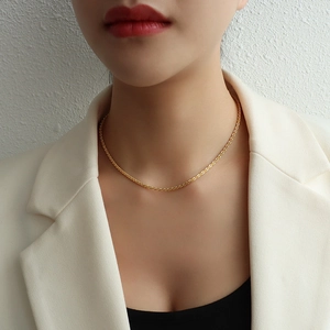 Collier chaîne torsadée dorée minimaliste pour femme porté avec un blazer blanc