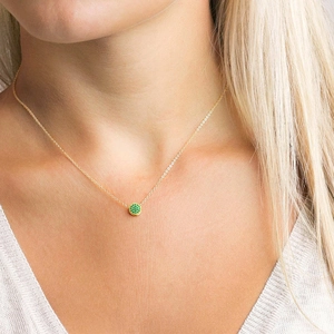 Close-up of elegant gold necklace featuring a dainty round pendant with green pavé crystals