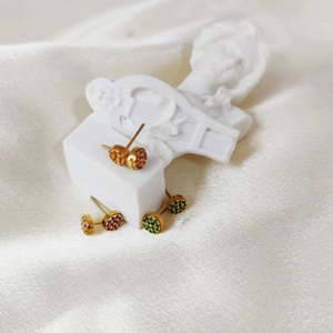 Close-up of three pairs of round gold-plated stud earrings with emerald, purple and orange crystals