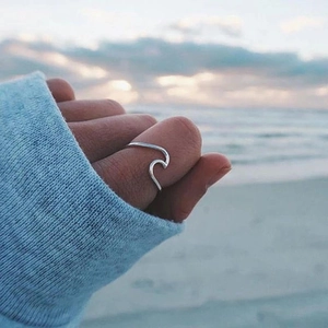 Minimalist wavy stainless steel open ring worn on thumb with scenic beach background