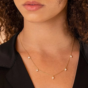 Detail of a minimalist gold necklace featuring five white pearl pendants on a female model