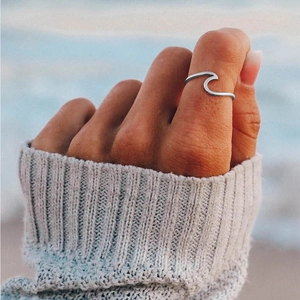 Minimalist wave-shaped 316L stainless steel ring worn on a model against a beach backdrop