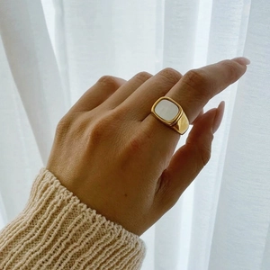 Gros plan d'une bague chevalière dorée avec insert blanc portée par un mannequin
