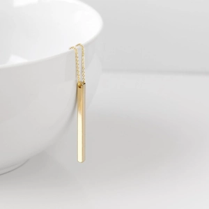 Detailed close-up of a minimalist vertical gold bar pendant necklace on a ceramic edge