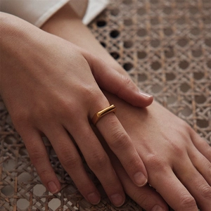 Close-up of a minimalist gold signet ring on a finger against a woven texture background