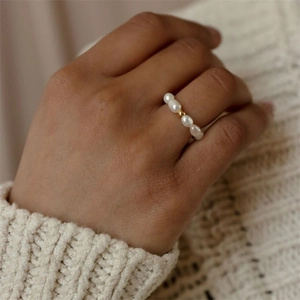 Minimalist oval pearl ring with a single gold bead on finger with a knit sweater