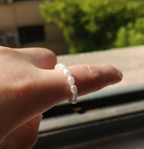 Close-up of minimalist stainless steel ring with small white freshwater pearls on a finger