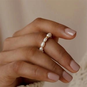 Detail of minimalist gold bead and oval pearl ring worn on model finger
