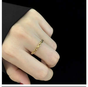 Macro shot of gold-plated oval link chain ring on model hand with minimalist black background