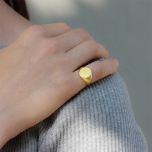 Minimalist gold signet ring featuring a polished round flat top worn on finger