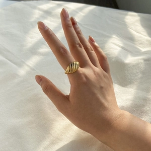 Détail d'une bague torsadée dorée portée à la main sur un fond de tissu blanc doux