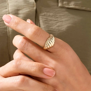 Gros plan sur une bague torsadée dorée portée à la main avec fond en tissu vert