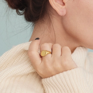 Close-up of a polished gold oval signet ring worn over a white knitted sweater