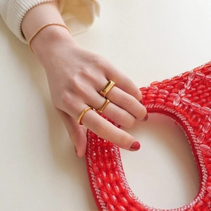 Detail of geometric gold ring set and tennis bracelet styled with a red beaded bag