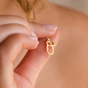 Close-up of gold-plated letter O pendant with heart charm on a minimalist chain