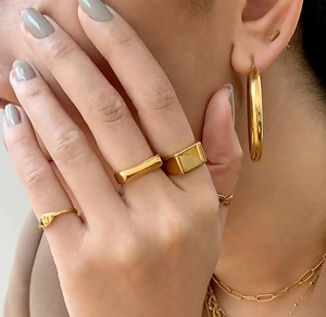 Close-up of a model wearing stacked gold stainless steel rings and hoop earrings