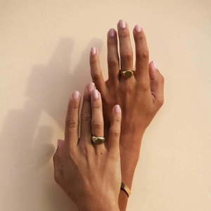 Close-up of minimalist gold-plated signet ring and thick band ring worn with a slim bracelet