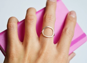 Close-up of minimalist silver geometric hollow ring on finger with pink notebook