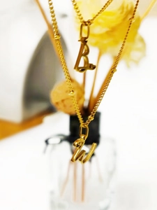 Détail de pendentifs lettres B et W dorés sur chaînes à perles avec fond floral