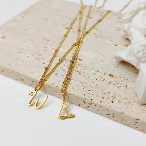 Détail de pendentifs lettres W et B plaqués or avec chaînes à billes sur plateau en pierre