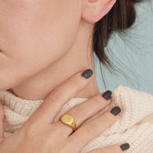 Polished gold round signet ring in stainless steel worn by model with cream sweater