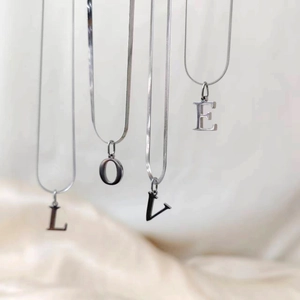 Detalle de collares de cadena de serpiente plateada con colgantes de letras LOVE sobre tela suave