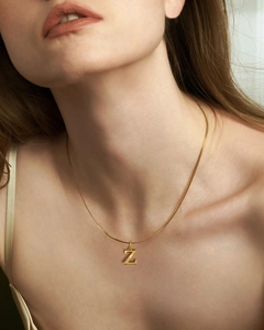 Detalle de una cadena de serpiente dorada con colgante de letra Z pulida en el cuello de modelo
